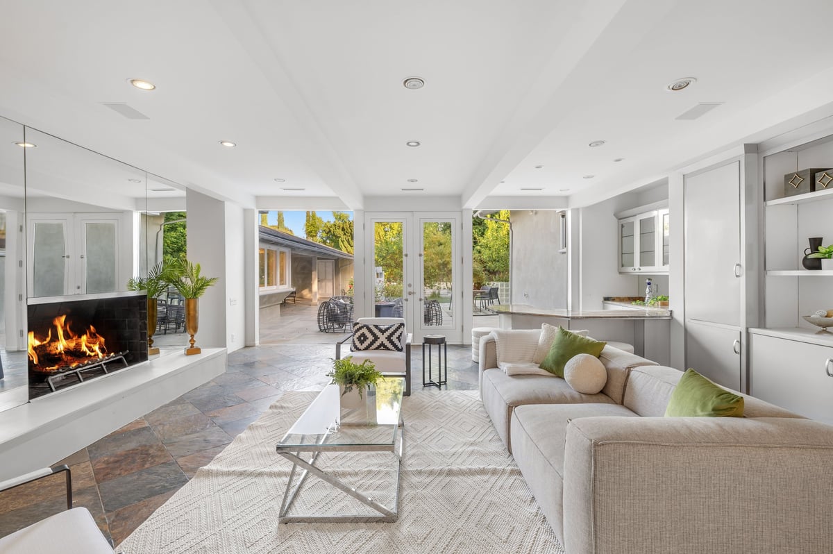 Minimal modern living room with beige sofa, fireplace, and glass doors opening to the outdoors